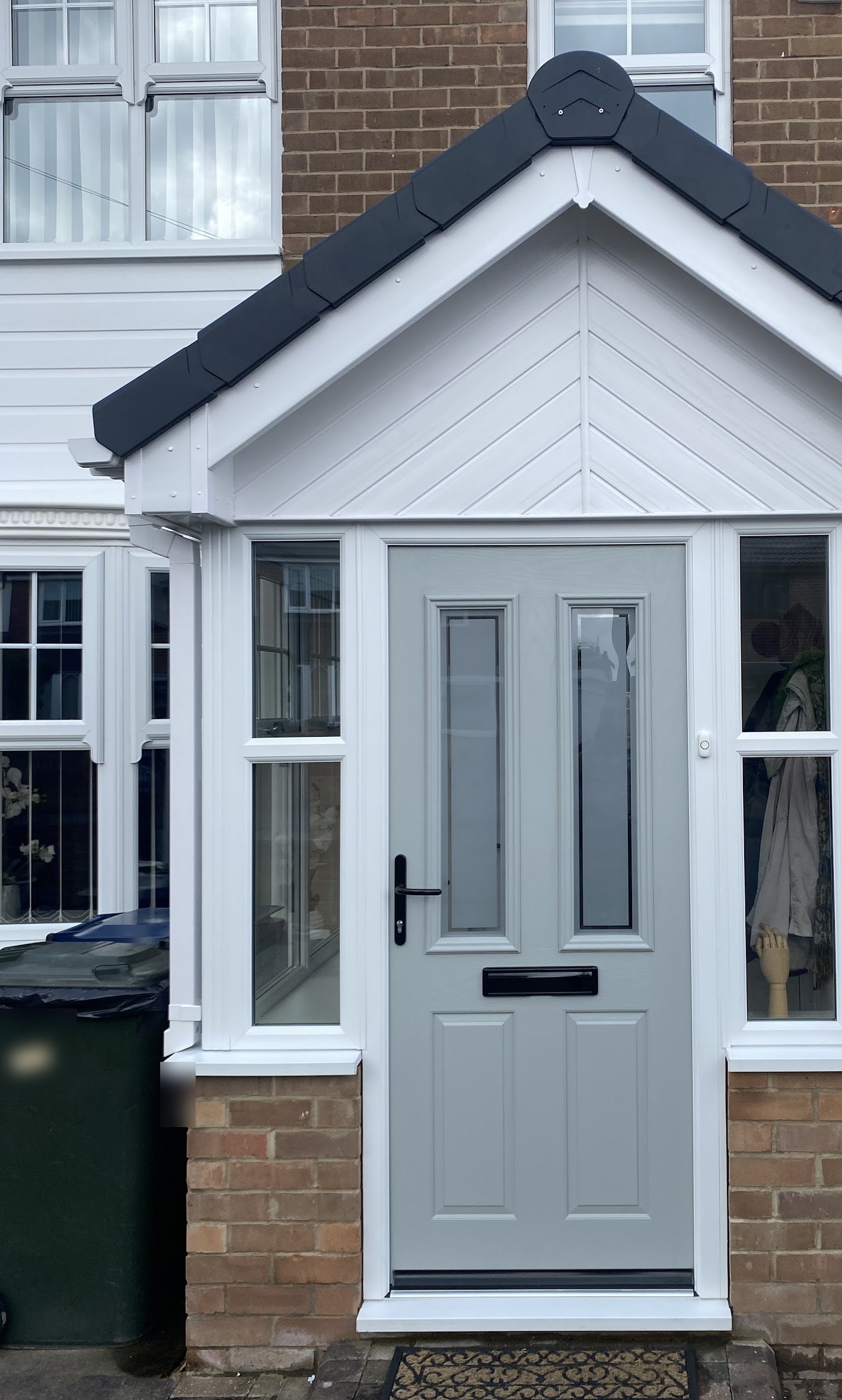 Grey composite front door inside a white uPVC porch with side lights