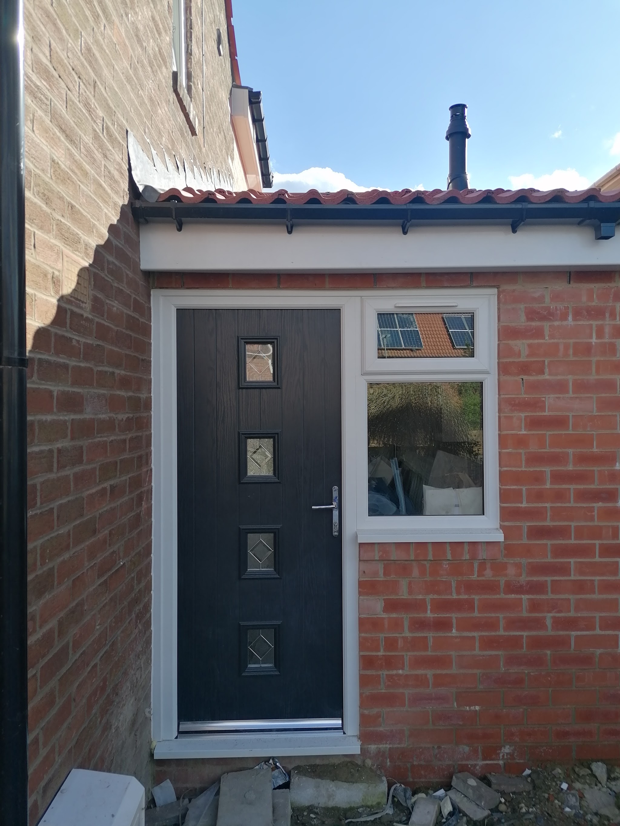 Black composite door and white uPVC window on a newly built brick extension